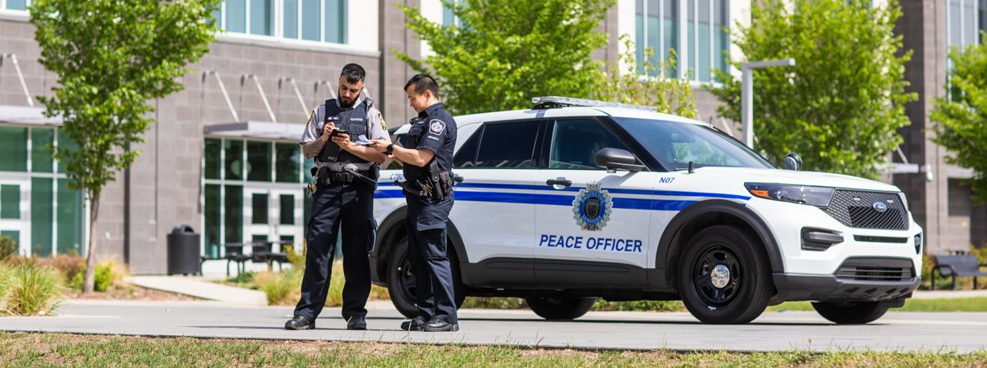 Two peace officers review notes beside police vehicle